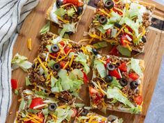 a wooden cutting board topped with slices of pizza covered in cheese and toppings on top of lettuce