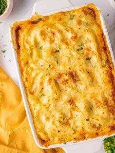 a casserole dish with cheese and parsley on the side next to broccoli