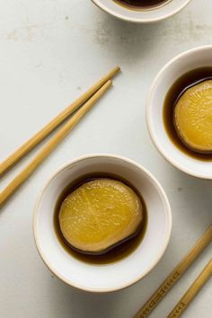 two white bowls filled with liquid next to chopsticks