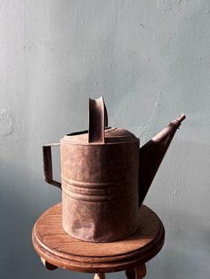 an old teapot sitting on top of a wooden table next to a gray wall