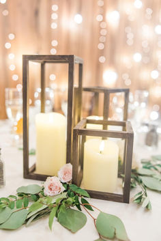 two candles are sitting on a table with greenery and pink roses in front of them