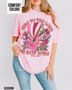 You will love our Comfort Colors Christian t shirt for women. It is based on the Bible verse Psalm 98:1. There is retro guitar and floral graphic on the front of this shirt.  This shirt would be great to wear to a Christian concert.  It is so trendy and cute and has a western flair. This is a great way to share your faith in Jesus with others. Comfort Colors T shirt Details: 100% ring-spun cotton Medium fabric (6.1 oz/yd² (206.8 g/m Relaxed fit Sewn-in twill label T shirt Care instructions: Mach Pink Relaxed Fit Band Merch T-shirt, Spring Concert T-shirt With Short Sleeves, Spring Music-themed Crew Neck T-shirt, Pink Band Merch T-shirt With Sublimation Print, Spring Concert T-shirt With Screen Print, Spring Concert Crew Neck T-shirt, Pink Screen Print Top For Concert, Pink T-shirt With Screen Print For Concert, Pink Screen Print T-shirt For Concert