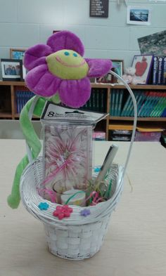 a stuffed animal sitting in a basket with scissors and flowers on the table next to bookshelves