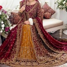 a woman in a red and gold bridal gown sitting on a couch with flowers behind her