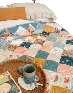 a coffee cup and book on a wicker tray next to a quilted bedspread