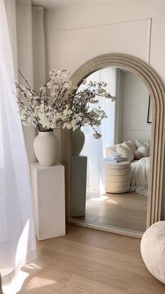 a vase filled with flowers sitting on top of a wooden floor next to a mirror