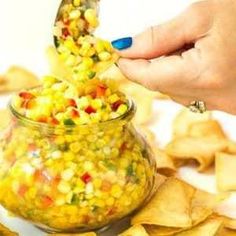 a person scooping corn into a jar filled with salsa and tortilla chips