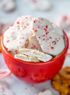 a red bowl filled with white frosting and sprinkles next to pretzels