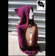 a purple and red knitted hooded blanket on top of a wooden stand in front of a building