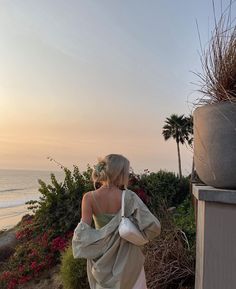 a woman in a white dress is walking on the beach with her back to the camera