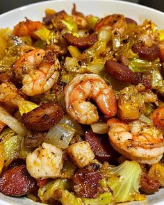 a white bowl filled with shrimp, sausage and veggies on top of a table