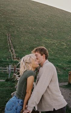 a man and woman kissing each other in front of a grassy hill on a sunny day