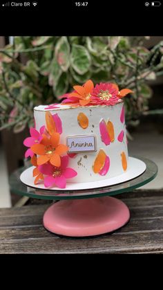 a white cake with orange and pink flowers on top, sitting on a wooden table