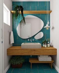 a bathroom with blue tiled walls and wooden counter top, mirror above the sink, potted plant on shelf next to it