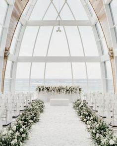 an indoor wedding setup with white flowers and greenery on the aisle, overlooking the ocean