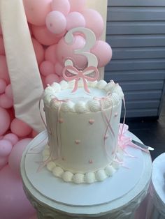 a three tiered cake sitting on top of a table next to pink and white balloons