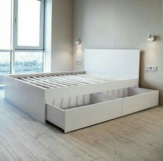 a white bed with drawers underneath it in a room next to a window and wooden floor