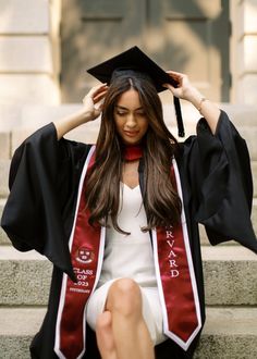 a woman sitting on steps wearing a graduation gown and holding her hair in the air