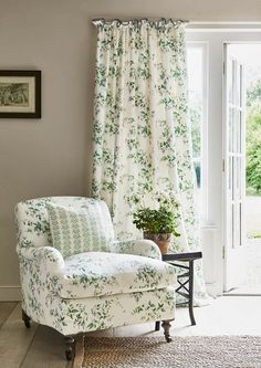 a white chair sitting in front of a window next to a green and white flowered curtain