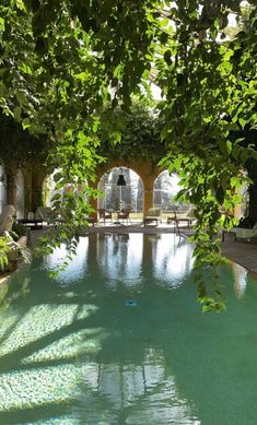 an outdoor swimming pool surrounded by greenery and stone arches with benches in the background