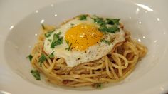 an egg on top of spaghetti in a white bowl