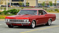 an old red car parked in a parking lot next to a shopping center with cars behind it