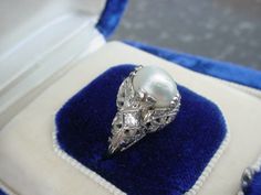 This is a lovely antique ring with a large pearl.  The pearl appears to be natural but has not been x-rayed and could be cultured.  The pearl measures about 7.85 mm's long by 6 mm's wide.  Hard to measure depth because there is a bar holding the back of the setting but approximately 6 mm's deep.  The setting is done in white gold with beautiful filigree details.  There are two tiny 2.5 mm diamond accents.  The current finger size is 6.75.  This ring may be resized within reason. This is a true a Vintage Ring Box, Curve Ring, Antique Ring, Tiny Diamond, Be Natural, Gold Filigree, Marquise Diamond, The Pearl, Multi Stone Ring