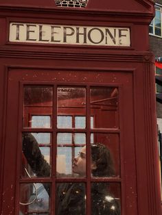 a woman is looking out the window of a red phone booth