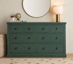 a green dresser with gold accents and a round mirror above the top, next to a lamp