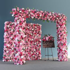 pink flowers are arranged on the side of a large flower wall with a welcome sign