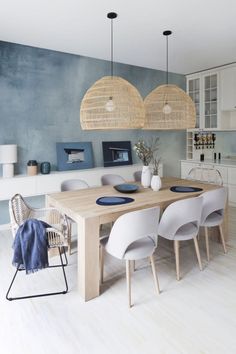 a dining room table and chairs in front of a blue wall with wicker hanging lights