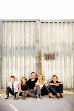 a family sitting on the ground in front of a metal wall with their arms around each other