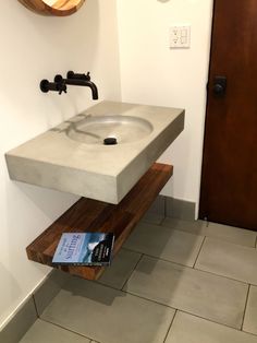 a bathroom sink sitting on top of a wooden shelf next to a book and mirror