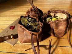 two brown leather bags filled with coins on top of a wooden floor