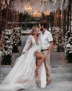 a man and woman are posing for a photo in front of an archway decorated with flowers