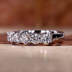 three stone diamond ring sitting on top of a piece of wood with leaves around it