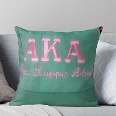 a green pillow with the letters aka written in pink on it sitting on a couch