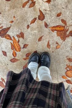 a person wearing black shoes and plaid pants standing on a floor with leaves all over it