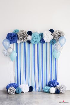 a blue and white striped backdrop with balloons, streamers and pom poms