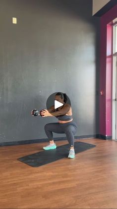 a woman squats on a yoga mat in front of a window and holds a camera