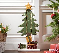 a wooden christmas tree with presents under it on the floor next to a basket full of gifts