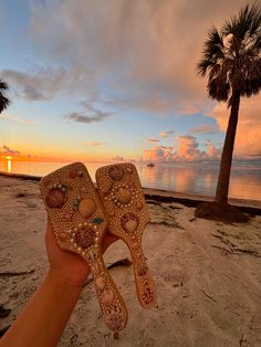 someone is holding up their flip flops on the beach at sunset with palm trees in the background