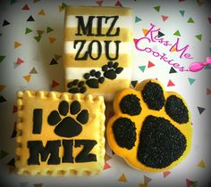 three decorated cookies with black and yellow icing on top of each cookie, one has a dog's paw