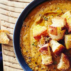 a blue bowl filled with soup and bread on top of a wooden table next to a piece of bread