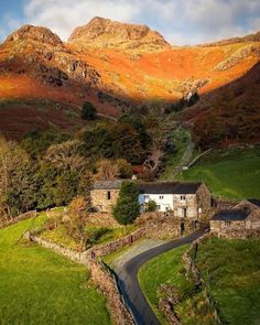 an old farm house in the mountains with a road going through it and a mountain behind it