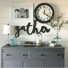 a gray dresser topped with a clock next to a lamp and pictures on the wall