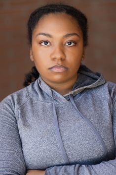 a woman with her arms crossed wearing a gray hoodie and looking at the camera