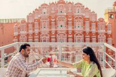 a man and woman sitting at a table with drinks in front of a pink building