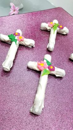 four white crosses with flowers on them sitting on a pink tablecloth covered in glitter