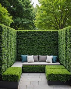 an outdoor seating area in the middle of a garden with green hedges and blue pillows